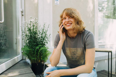 Happy woman talking on the phone while sitting near coffee shop