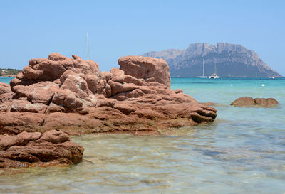 Rocks on sea shore against clear blue sky