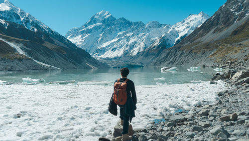 Rear view of man standing on snowcapped mountain against sky