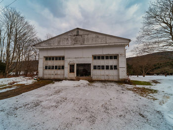 House on snow covered field by building against sky