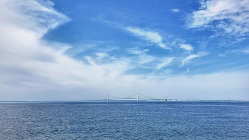 View of suspension bridge over sea against cloudy sky