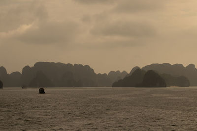 Scenic view of sea by silhouette mountain against sky