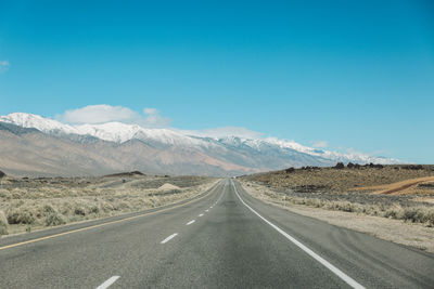 Empty road by mountains against clear blue sky