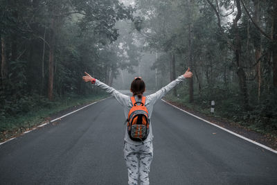 Rear view of woman standing on road in forest