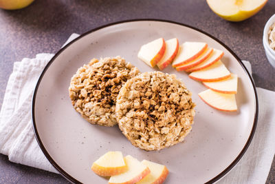 Appetizing crumble of apples and oatmeal on a plate and fruits on the table.