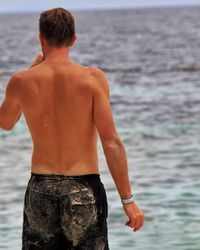 Rear view of shirtless man standing at beach