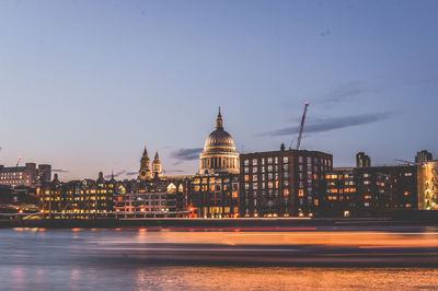 Light trails in river against historic church in illuminated city at dusk