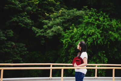 Woman standing by railing against trees