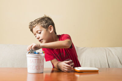 Boy sitting by table against wall