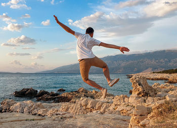 Rear view of man jumping in air on beach. summer, sea, shore, freedom.