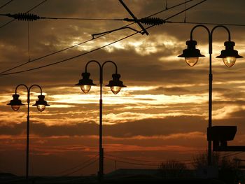 Low angle view of power lines against cloudy sky during sunset