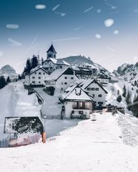 Snow covered houses by buildings against sky