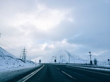 Empty road by snowcapped mountain against sky