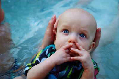 Cropped hand of person holding cute baby girl in swimming in pool