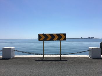 Road sign by sea against clear blue sky