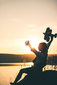 Girl sitting on rock at lakeshore during sunset