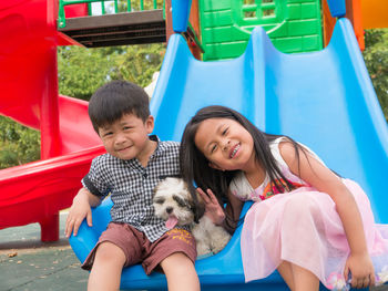 Portrait of smiling siblings with dog sitting on slide 