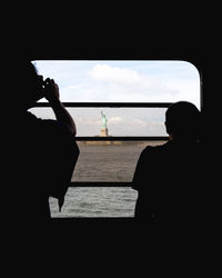 Rear view of silhouette people sitting by sea against sky