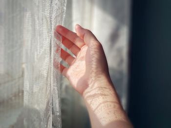 Close-up of hand touching curtain at home