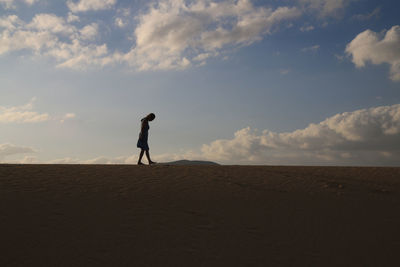 Woman walking on sand at beach against sky