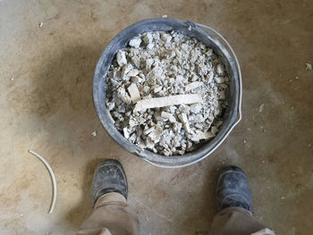 Low section of man standing by broken concrete in bucket on floor