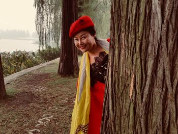 Portrait of woman smiling while hiding behind tree trunk