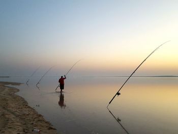 Silhouette man fishing by sea against clear sky