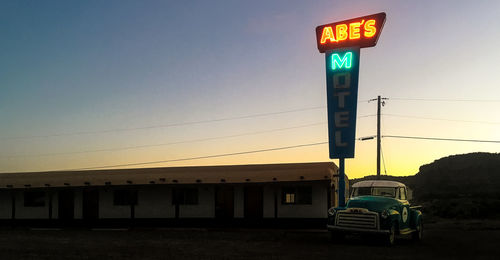 Illuminated information sign against clear sky during sunset