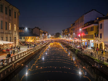 People on illuminated street amidst buildings in city rivera at night