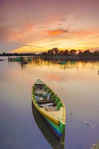 Boat moored in lake against sky during sunset