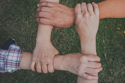 Cropped image of friends holding hands against grass