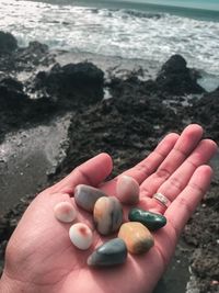 Cropped image of hand holding pebbles at beach
