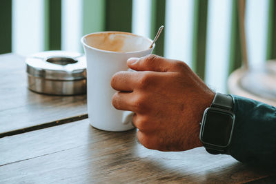 Midsection of man holding coffee cup on table