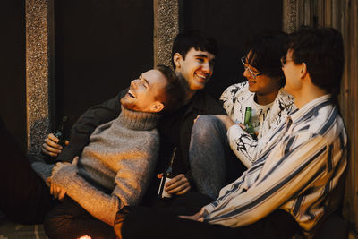 Happy male friends chilling with beer bottles while sitting at balcony