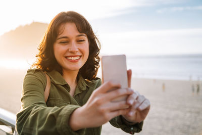 Portrait of smiling young man using smart phone against sky