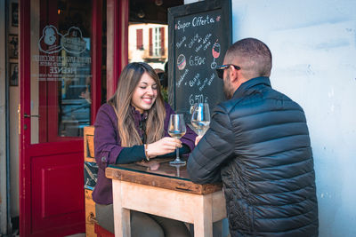 Couple holding wineglasses on table talking while sitting at outdoor cafe