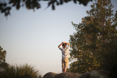 Rear view of boy with hands behind head standing on hay bale at field