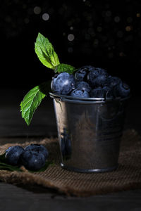 Mini gray bucket full of fresh blueberries with mint leaves, laid on top of a jute piece with rustic 