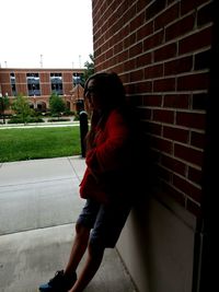 Side view of woman standing against brick wall