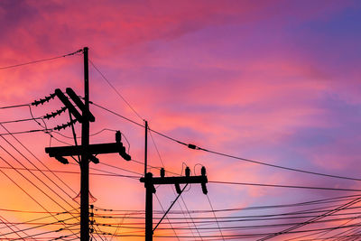 Low angle view of silhouette electricity pylon against dramatic sky