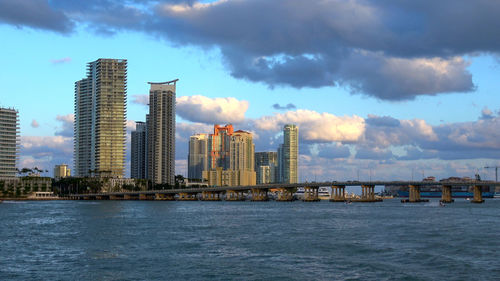 Sea by modern buildings against sky in city