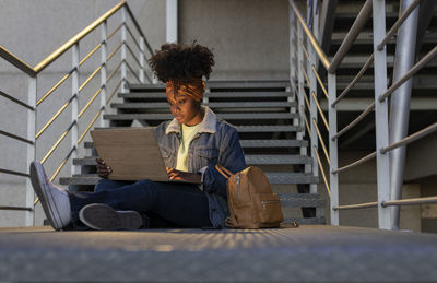 Young woman using laptop sitting on staircase at night