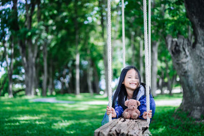 Portrait of smiling girl sitting on grass against trees