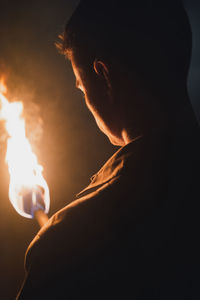 Back view of cropped anonymous male speleologist with flaming torch standing in dark narrow rocky cave while exploring subterranean environment