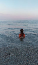 Man in sea against sky during sunset