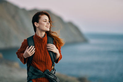 Young woman looking away while standing in sea against sky