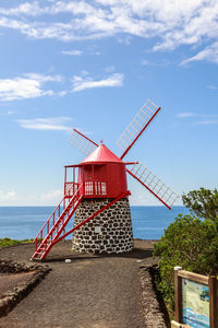 Traditional windmill on beach by sea against sky