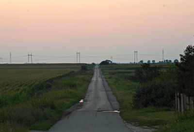 Empty road amidst field against sky during sunset