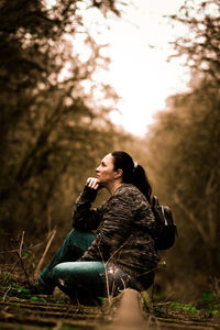 Side view of young woman sitting in forest