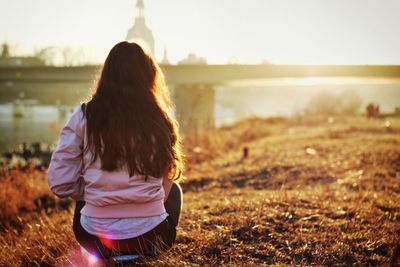 Rear view of woman standing on field against sunset sky